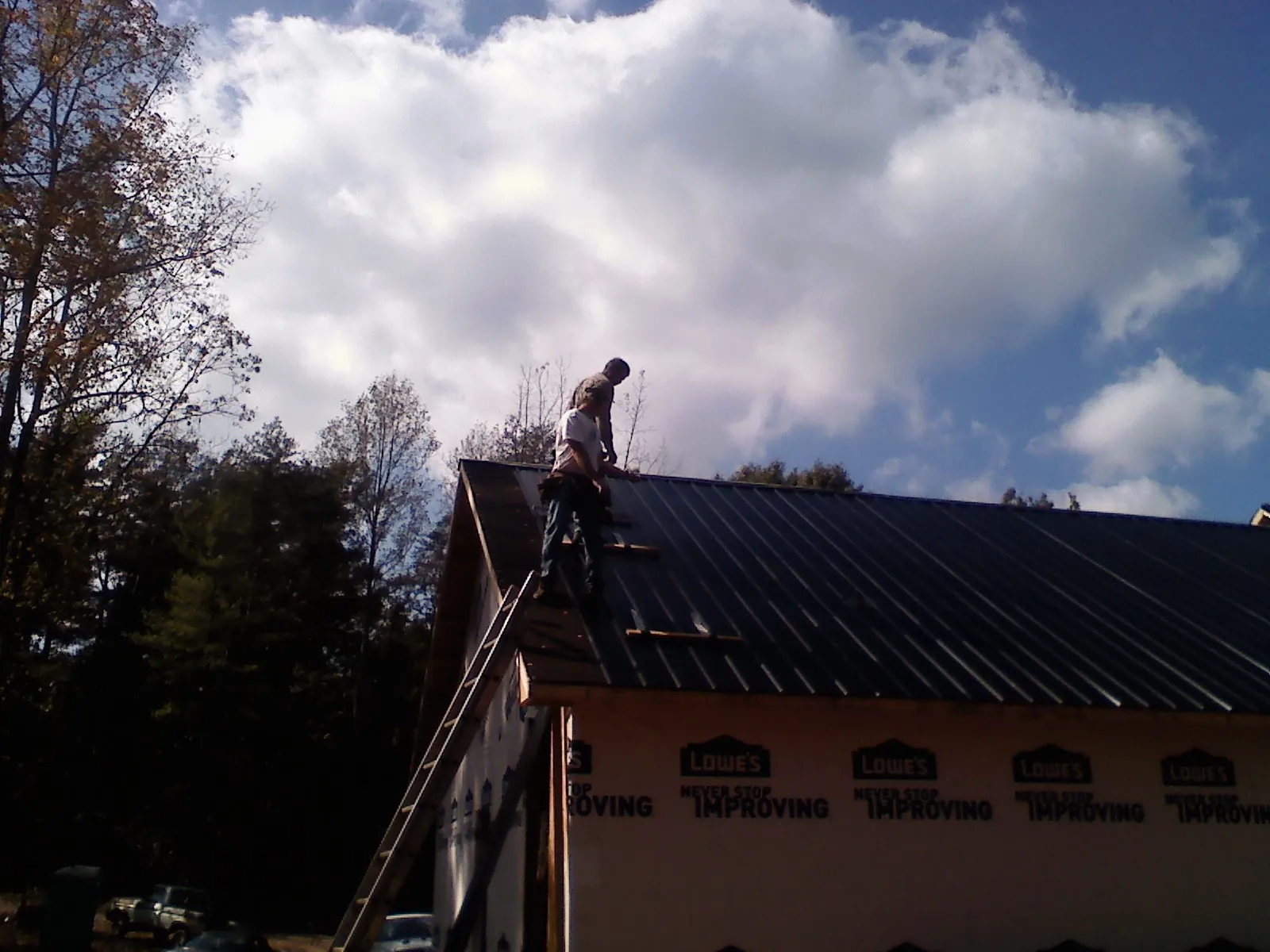 Roofer fastening dark metal panels high against a cloudy sky, from a Roof Inspection job in Montgomery