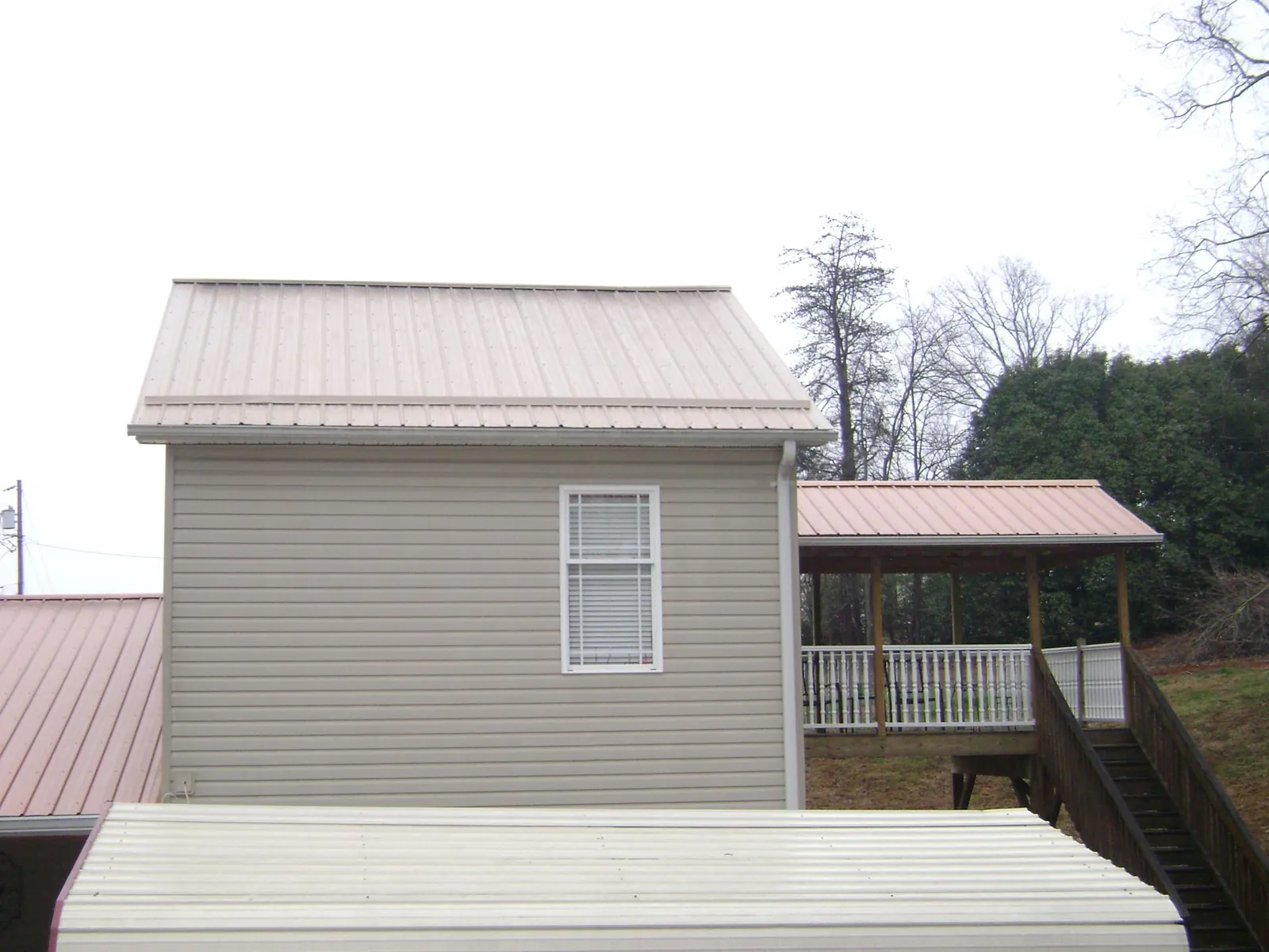 Tan metal roofs on a two story addition and attached porch, from a Roof Replacement job in Montgomery